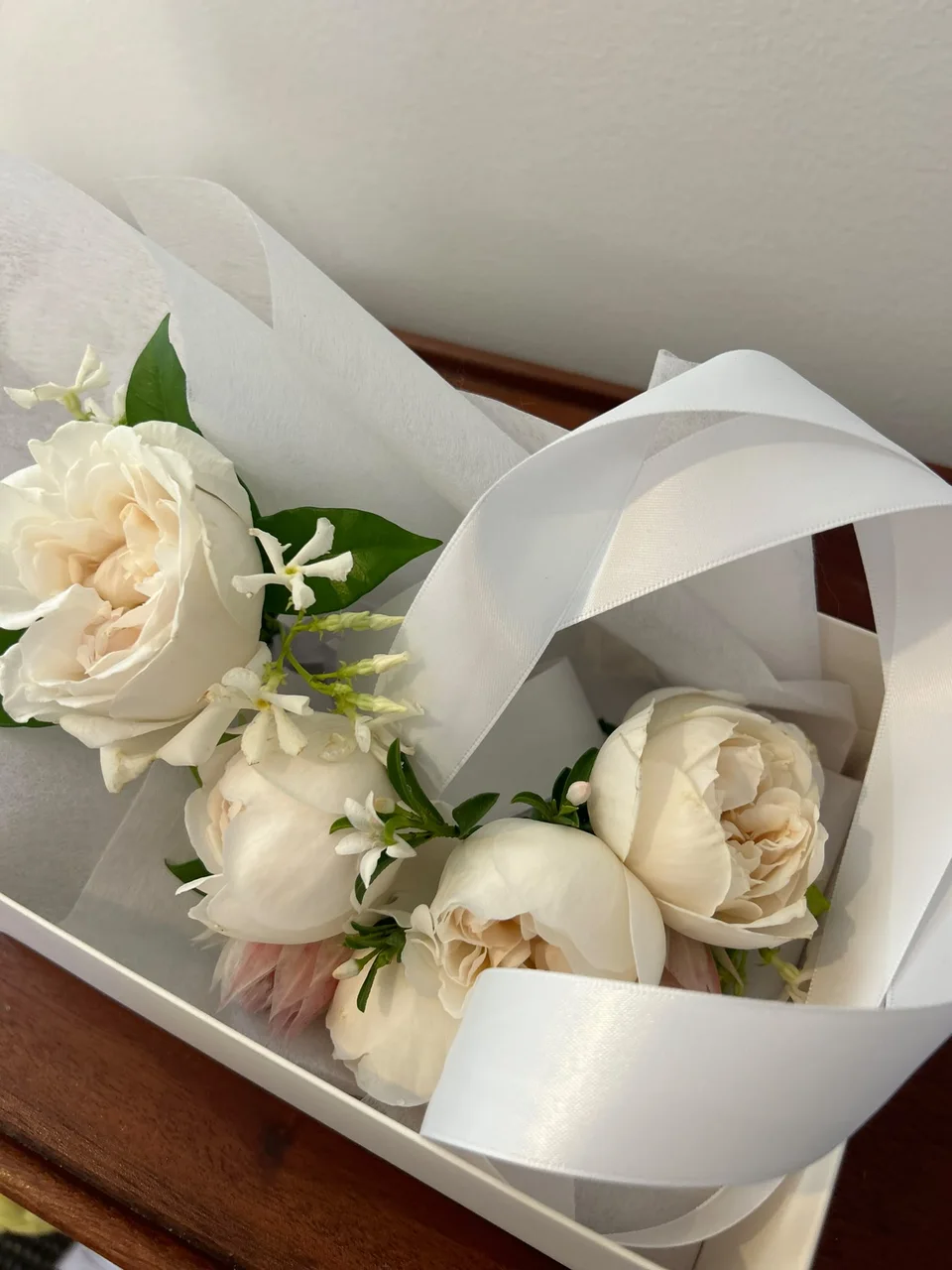 Ivory garden roses and delicate white flowers carefully nestled in tissue and satin ribbon